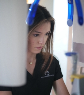 Sutton Dentistry Focused view of a female dental professional wearing a black Sutton Dentistry uniform, working near dental equipment.